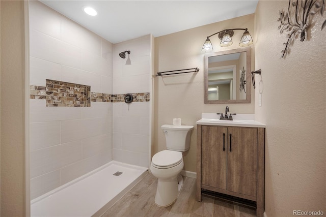 bathroom featuring tiled shower, hardwood / wood-style floors, vanity, and toilet