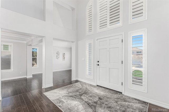 foyer with a towering ceiling, crown molding, baseboards, and wood-type flooring