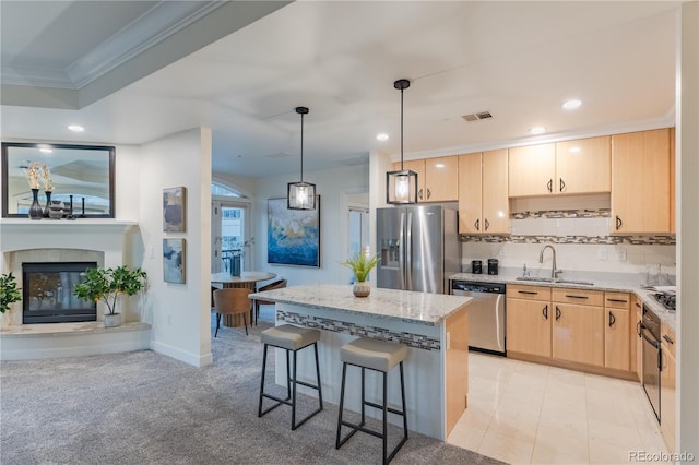 kitchen with sink, decorative light fixtures, appliances with stainless steel finishes, light brown cabinetry, and light stone countertops