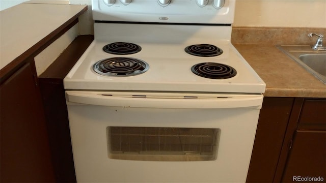 interior details with electric range, sink, and dark brown cabinets