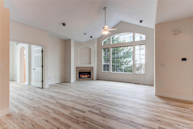 unfurnished living room with ceiling fan, high vaulted ceiling, light wood finished floors, and a tile fireplace