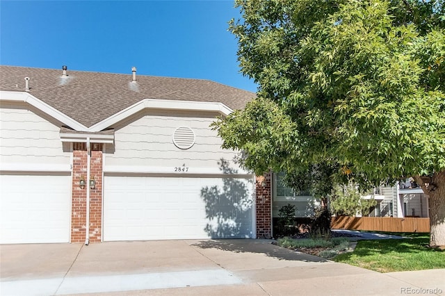 view of front facade featuring fence, driveway, roof with shingles, an attached garage, and brick siding