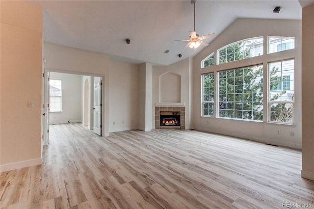 unfurnished living room featuring baseboards, light wood-type flooring, a tile fireplace, high vaulted ceiling, and a ceiling fan