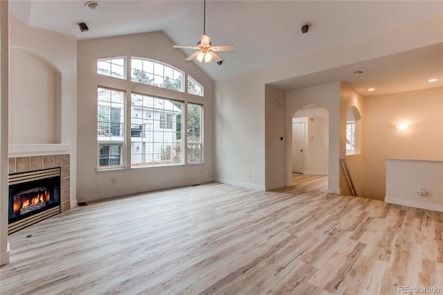 unfurnished living room with a tile fireplace, wood finished floors, arched walkways, high vaulted ceiling, and a ceiling fan