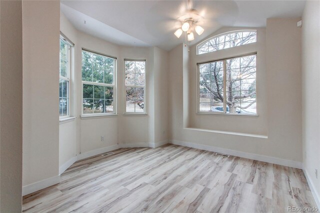 empty room featuring lofted ceiling, plenty of natural light, wood finished floors, and visible vents