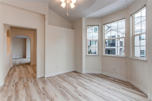 spare room featuring baseboards, visible vents, lofted ceiling, arched walkways, and light wood-style floors