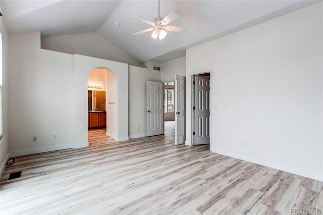 unfurnished bedroom featuring light wood-style flooring, arched walkways, ensuite bathroom, and high vaulted ceiling