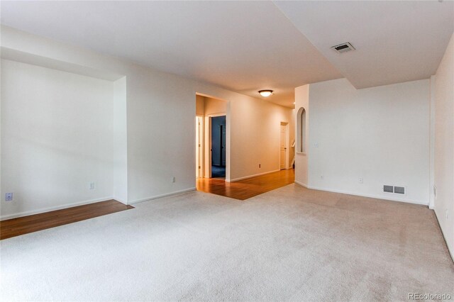 carpeted empty room featuring visible vents, arched walkways, and baseboards