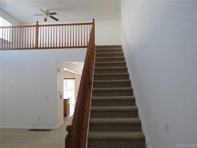 staircase featuring a towering ceiling, baseboards, visible vents, a ceiling fan, and carpet