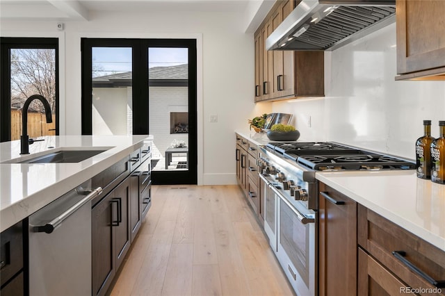 1195 S Milwaukee St, Denver, CO 80210 - kitchen featuring a sink, wall chimney exhaust hood, appliances with stainless steel finishes, light wood-style floors, and light countertops