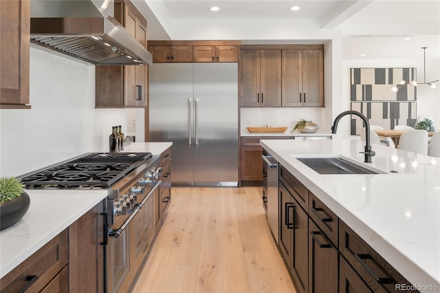 1195 S Milwaukee St, Denver, CO 80210 - kitchen with a sink, high quality appliances, wall chimney range hood, light wood-style flooring, and recessed lighting