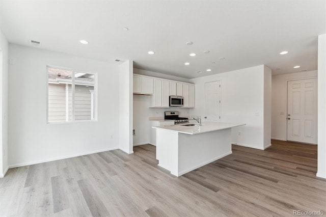 kitchen with sink, stainless steel appliances, light hardwood / wood-style floors, white cabinets, and a center island with sink