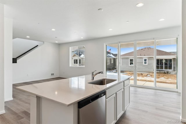 kitchen with a kitchen island with sink, sink, stainless steel dishwasher, and light wood-type flooring