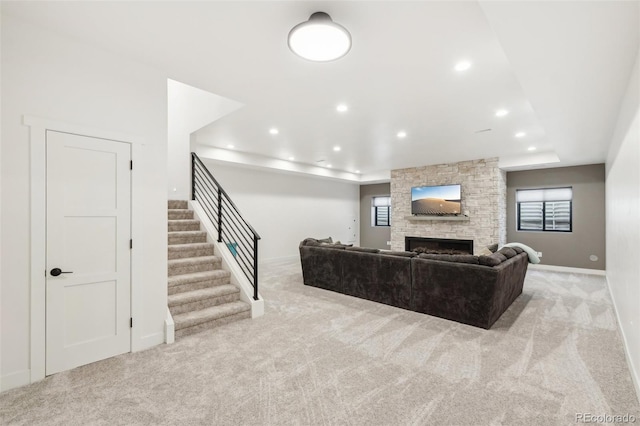 living room with light colored carpet, a tray ceiling, a stone fireplace, and a healthy amount of sunlight