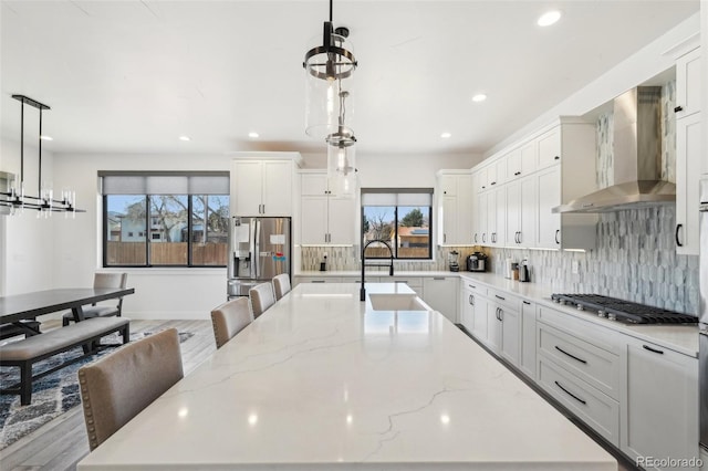 kitchen featuring appliances with stainless steel finishes, wall chimney exhaust hood, hanging light fixtures, and a spacious island