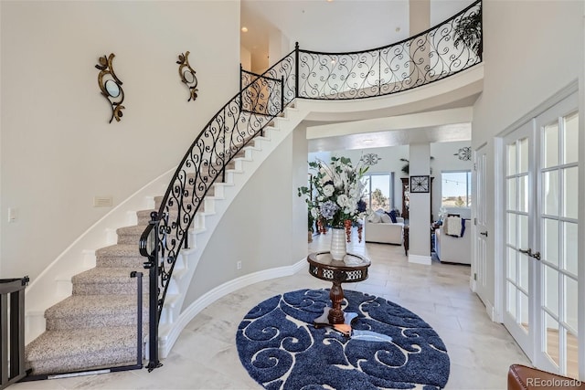 entryway featuring stairs, french doors, a towering ceiling, and baseboards