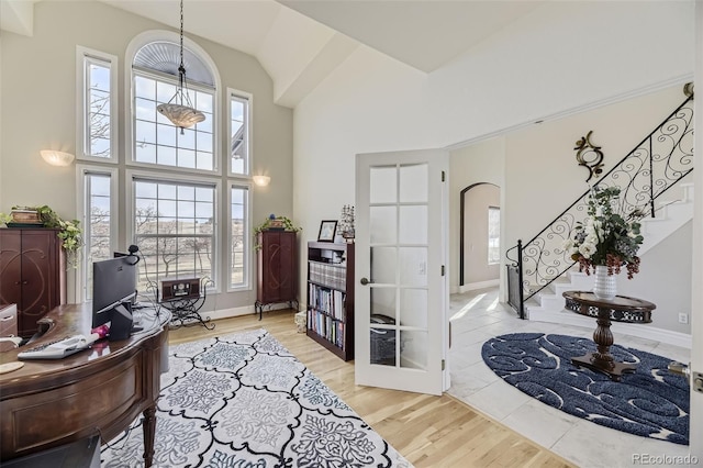 entrance foyer with arched walkways, light wood-style floors, high vaulted ceiling, baseboards, and stairs