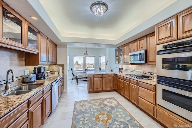 kitchen featuring decorative backsplash, a raised ceiling, a peninsula, stainless steel appliances, and a sink