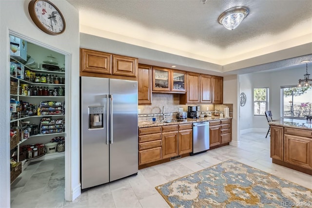 kitchen featuring brown cabinets, stainless steel appliances, backsplash, glass insert cabinets, and a sink