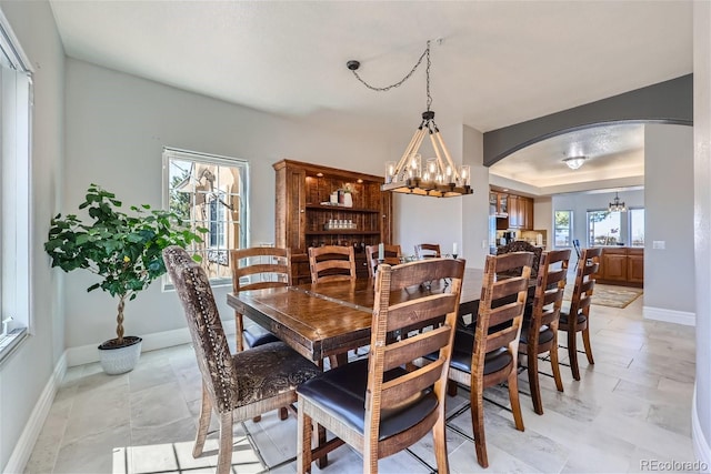 dining room with baseboards, a chandelier, arched walkways, and a raised ceiling