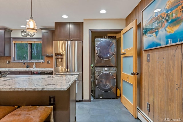 kitchen featuring decorative light fixtures, stainless steel refrigerator with ice dispenser, decorative backsplash, stacked washer and dryer, and light stone counters