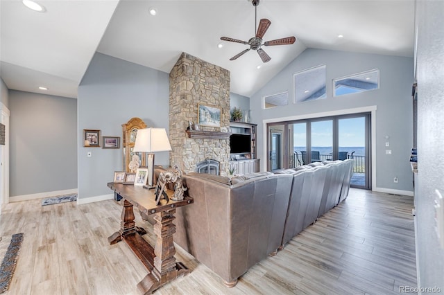 living room with a stone fireplace, ceiling fan, high vaulted ceiling, and light wood-type flooring