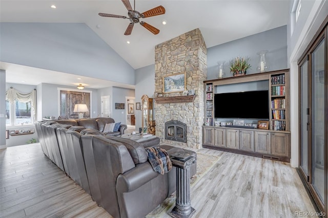 living room featuring ceiling fan, light wood-type flooring, a fireplace, and high vaulted ceiling