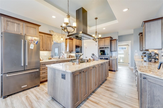 kitchen with stainless steel appliances, island range hood, decorative light fixtures, an inviting chandelier, and an island with sink