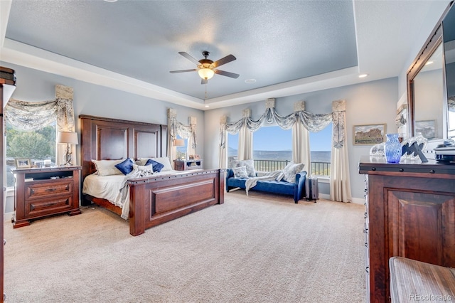 carpeted bedroom with a textured ceiling, a tray ceiling, and ceiling fan