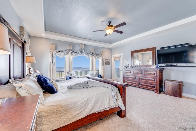 carpeted bedroom featuring ceiling fan, a textured ceiling, access to outside, and a tray ceiling