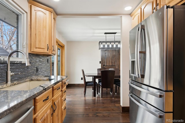 kitchen with appliances with stainless steel finishes, dark stone counters, pendant lighting, sink, and backsplash