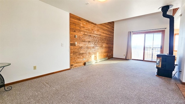 living room with carpet floors, a baseboard heating unit, wood walls, and a wood stove