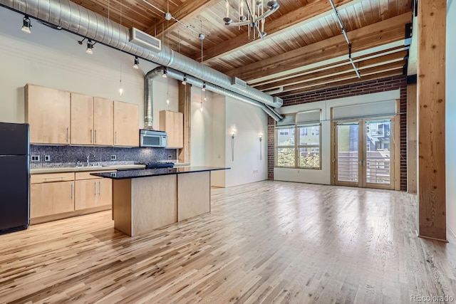 kitchen featuring beamed ceiling, a kitchen island, light hardwood / wood-style flooring, light brown cabinets, and black refrigerator