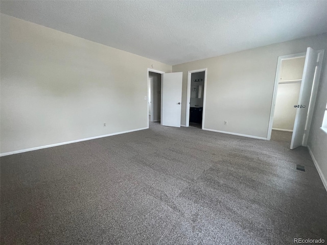 unfurnished bedroom featuring a textured ceiling, a spacious closet, and dark colored carpet