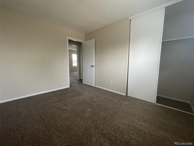 unfurnished bedroom with a closet, a textured ceiling, and dark colored carpet