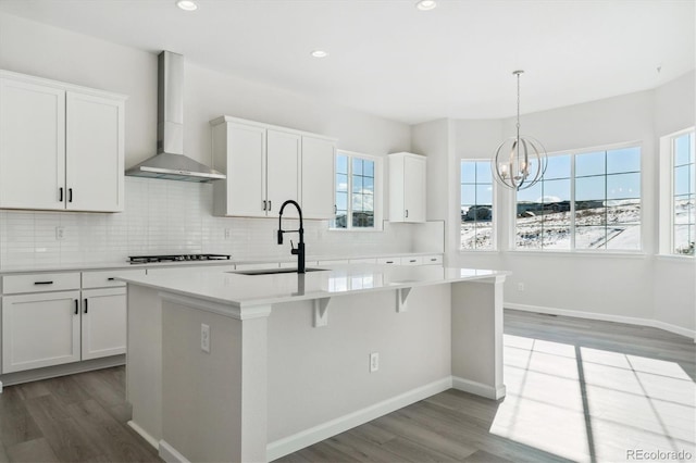 kitchen featuring white cabinets, a kitchen island with sink, sink, and wall chimney exhaust hood