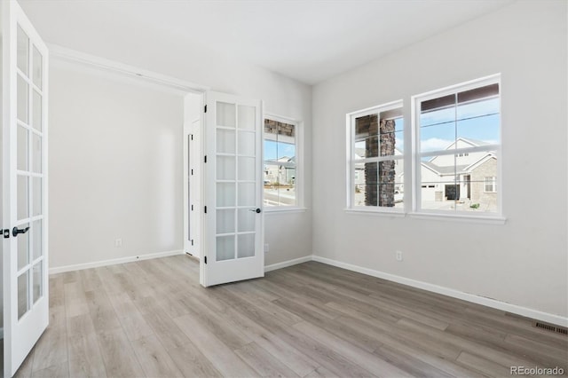 empty room featuring plenty of natural light, light hardwood / wood-style floors, and french doors