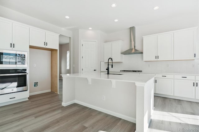 kitchen featuring sink, white cabinetry, a kitchen island with sink, and wall chimney range hood