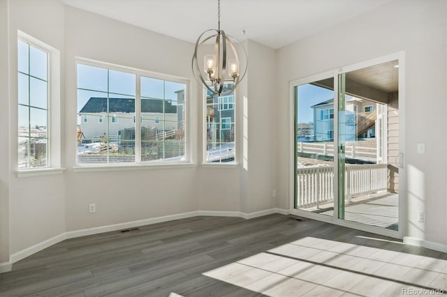 unfurnished dining area featuring a chandelier, plenty of natural light, and dark wood-type flooring