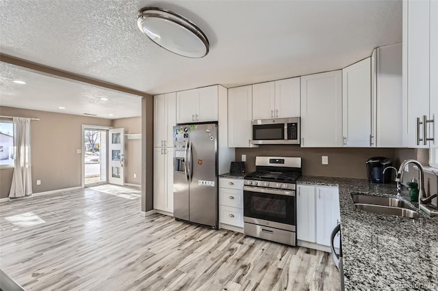 kitchen featuring a textured ceiling, stainless steel appliances, sink, dark stone countertops, and white cabinetry