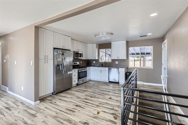 kitchen with white cabinets, sink, stainless steel appliances, and light hardwood / wood-style flooring