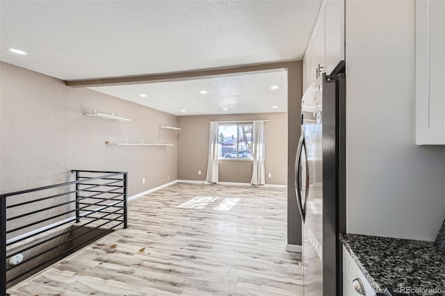 kitchen with white cabinetry, light hardwood / wood-style flooring, beamed ceiling, dark stone countertops, and stainless steel fridge