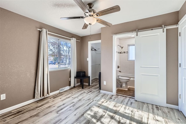 unfurnished bedroom featuring a walk in closet, ceiling fan, a barn door, light wood-type flooring, and a closet