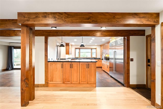 kitchen featuring built in refrigerator, dark countertops, healthy amount of natural light, beam ceiling, and a peninsula