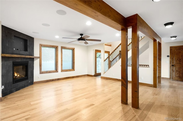 unfurnished living room with light wood-style flooring, a ceiling fan, baseboards, a tile fireplace, and stairway