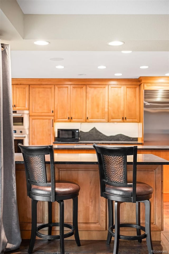 kitchen with double oven, recessed lighting, a kitchen breakfast bar, and dark wood finished floors