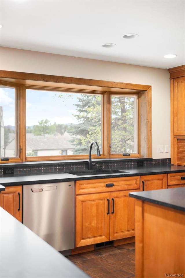 kitchen with stainless steel dishwasher, a sink, dark countertops, brown cabinetry, and recessed lighting