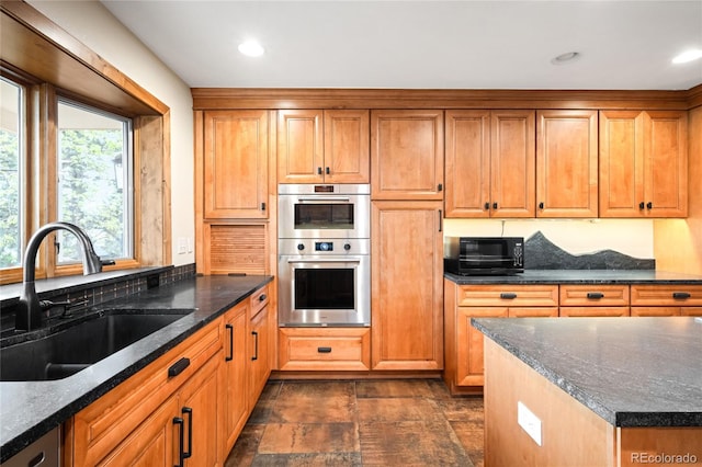 kitchen featuring a sink, stainless steel double oven, dark stone counters, brown cabinets, and recessed lighting