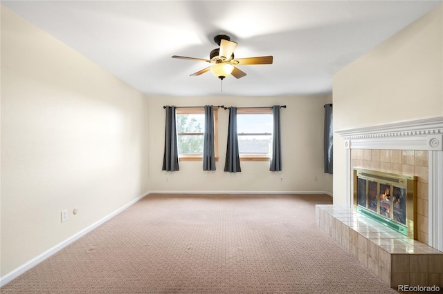 unfurnished living room featuring ceiling fan, carpet flooring, a tiled fireplace, and baseboards