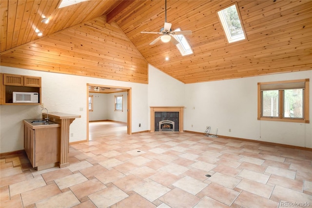 unfurnished living room featuring high vaulted ceiling, wood ceiling, a skylight, ceiling fan, and a tiled fireplace
